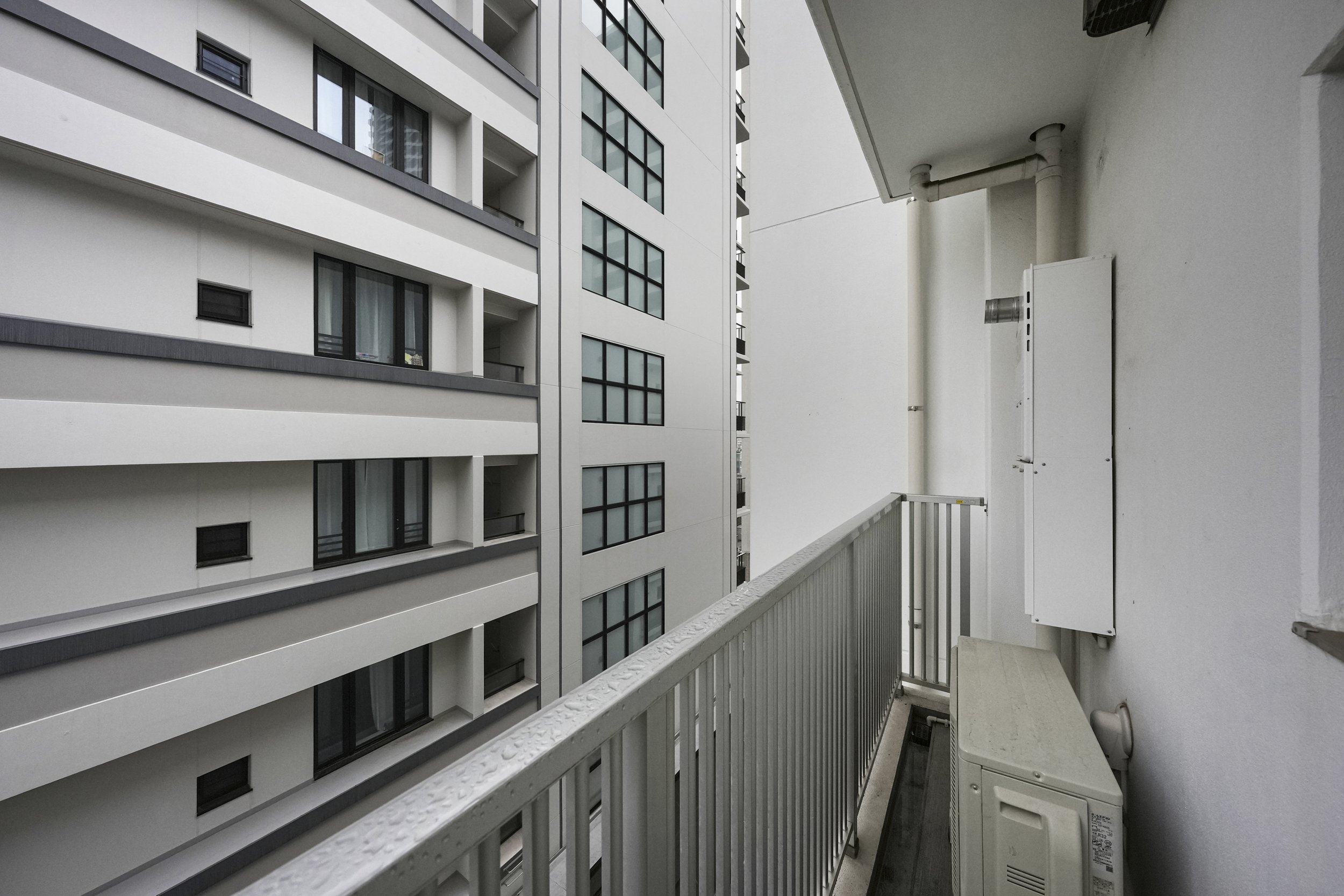 高層マンションのバルコニーからの景色。隣の建物の白い壁と窓が見える。