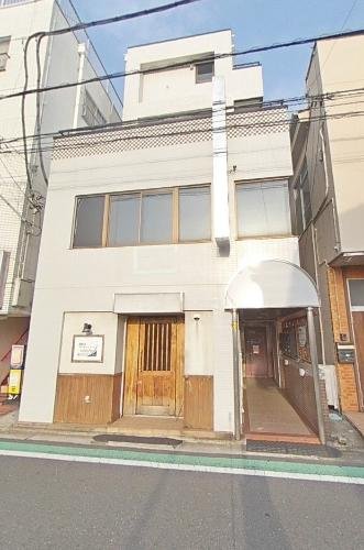 白い3階建てのビル。木製の扉と入口のアーチ型の屋根がある。