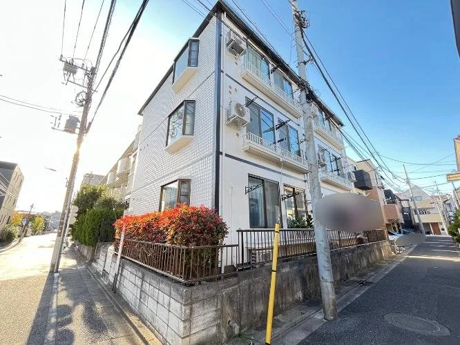 四階建ての白いマンションと狭い通りに電柱と電線がある街の風景