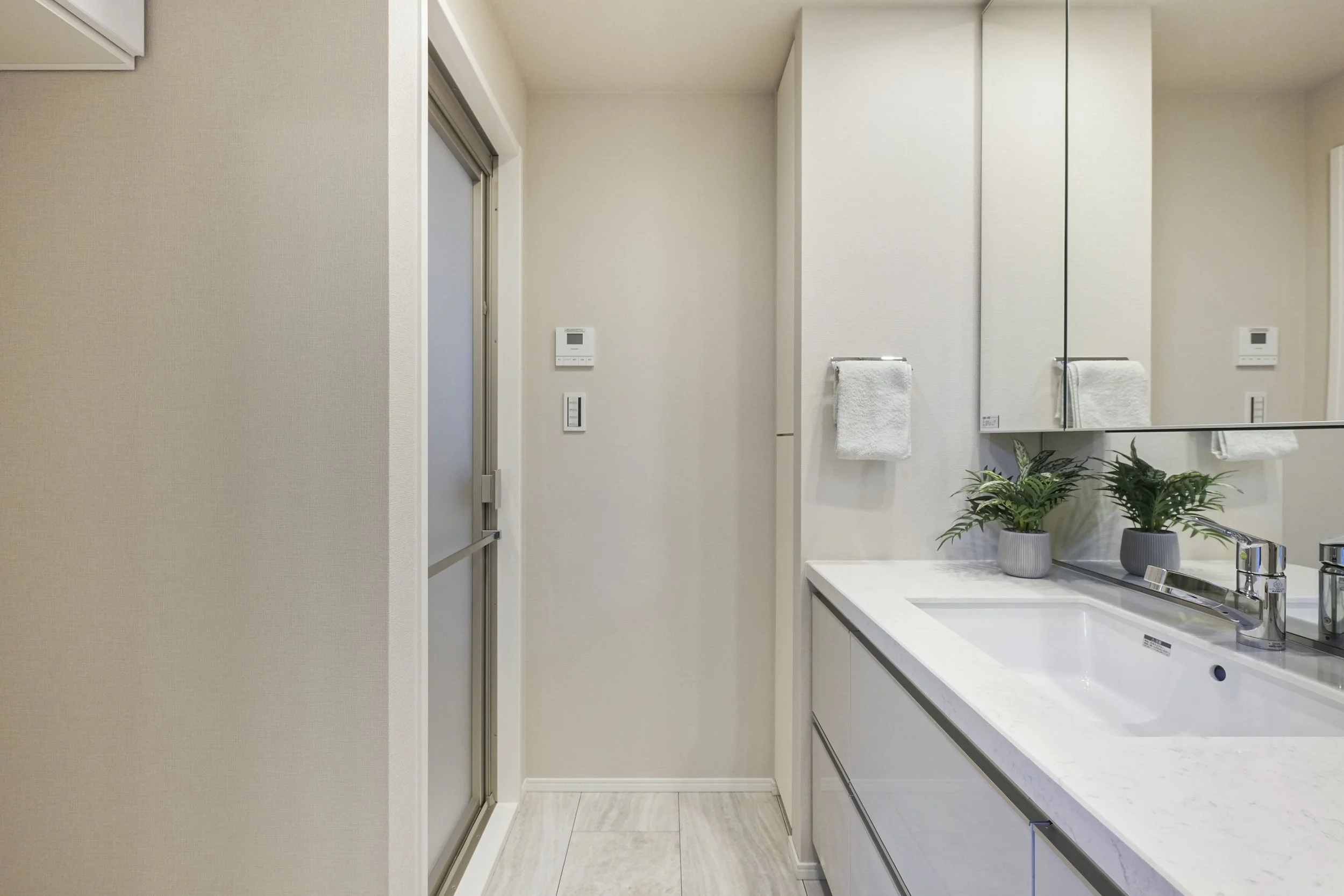 白い洗面台と鏡、壁にタオル掛けと植物、洗面所の鏡の反射