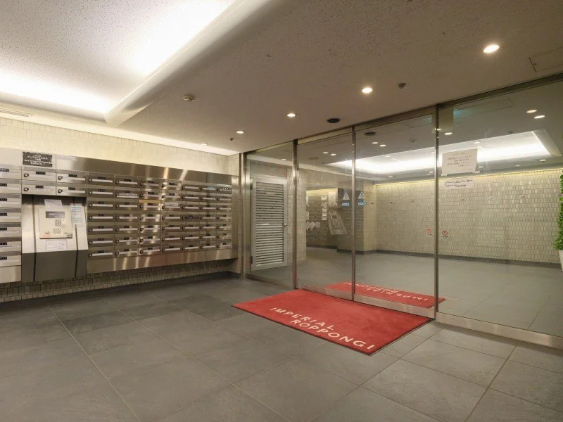 集合ポストとガラス扉、赤いマットが入口に置かれているエントランスホール