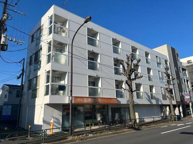 白色の多層建築のアパートメントまたはレジデンス。窓とバルコニーが各階にあり、建物の前に木の整頓された木が並んでいる。