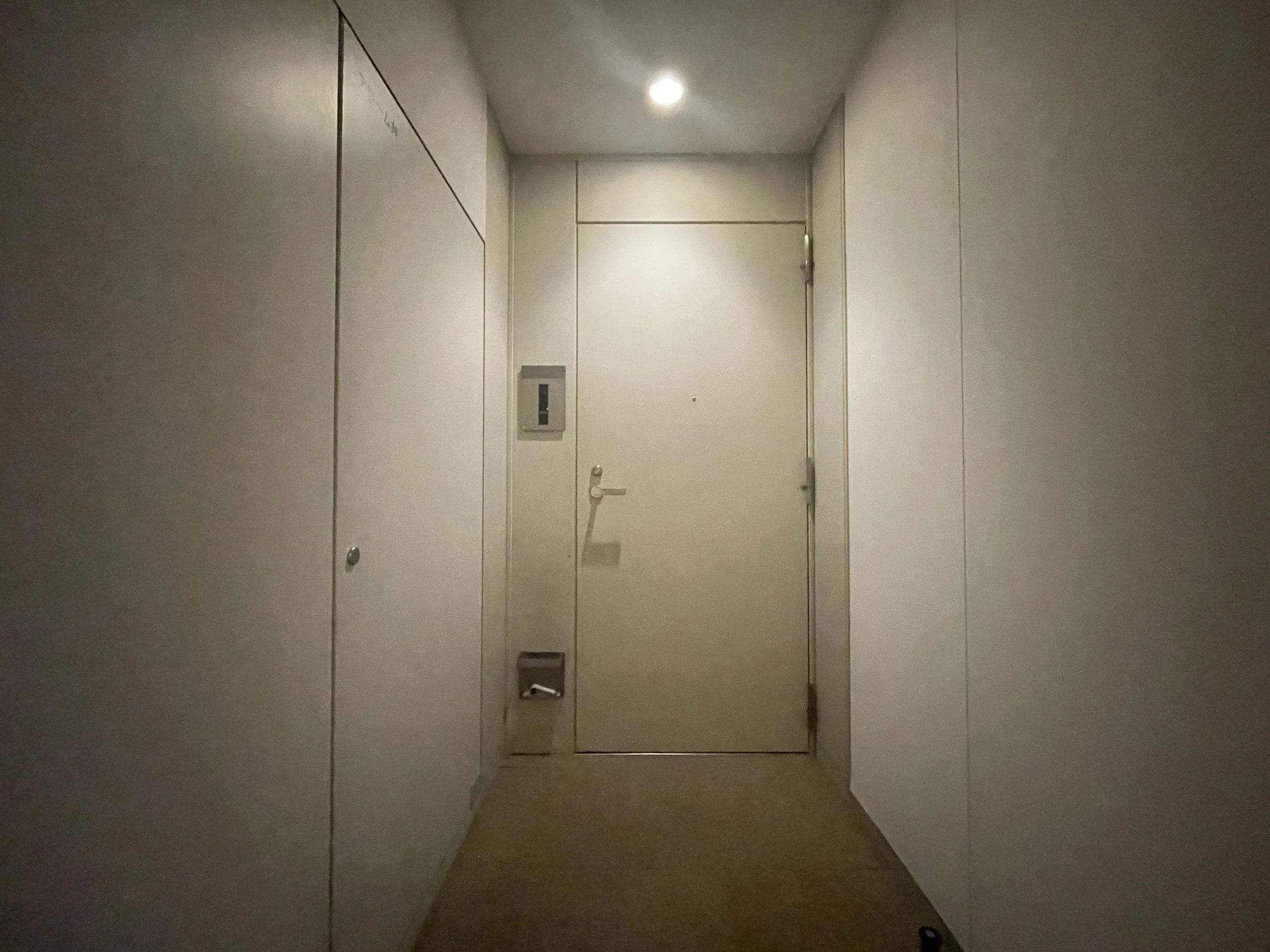 エレベーターの入り口の扉が閉まった廊下の様子。壁は白色で、照明が天井に点灯している。