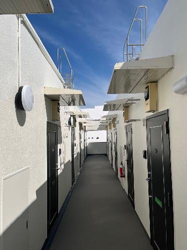 白い建物の廊下に複数のドアと屋上への階段が見える