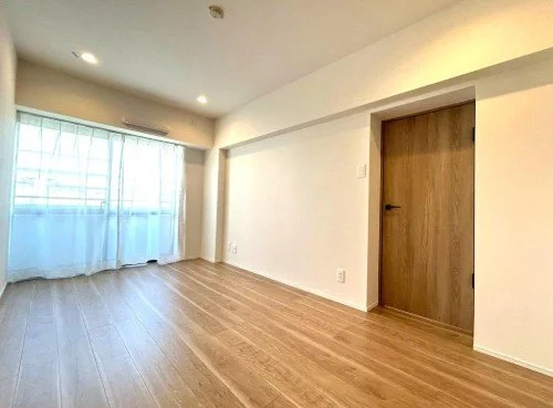 白い壁と木製のドアがある空のリビングルーム、木製のフローリングと窓にカーテンがついている