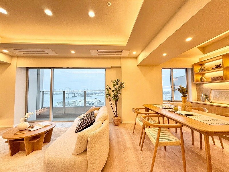 明るくて広々としたリビングルームとダイニングエリア。大きな窓から都市の景色が見える、現代的なインテリア。カウンターテーブルには花や食器が飾られている。