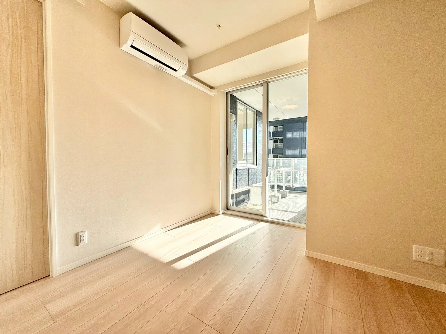 明るい室内の部屋、木製のフローリングと壁、扉と窓、バルコニーにつながるフェンスと建物の外観