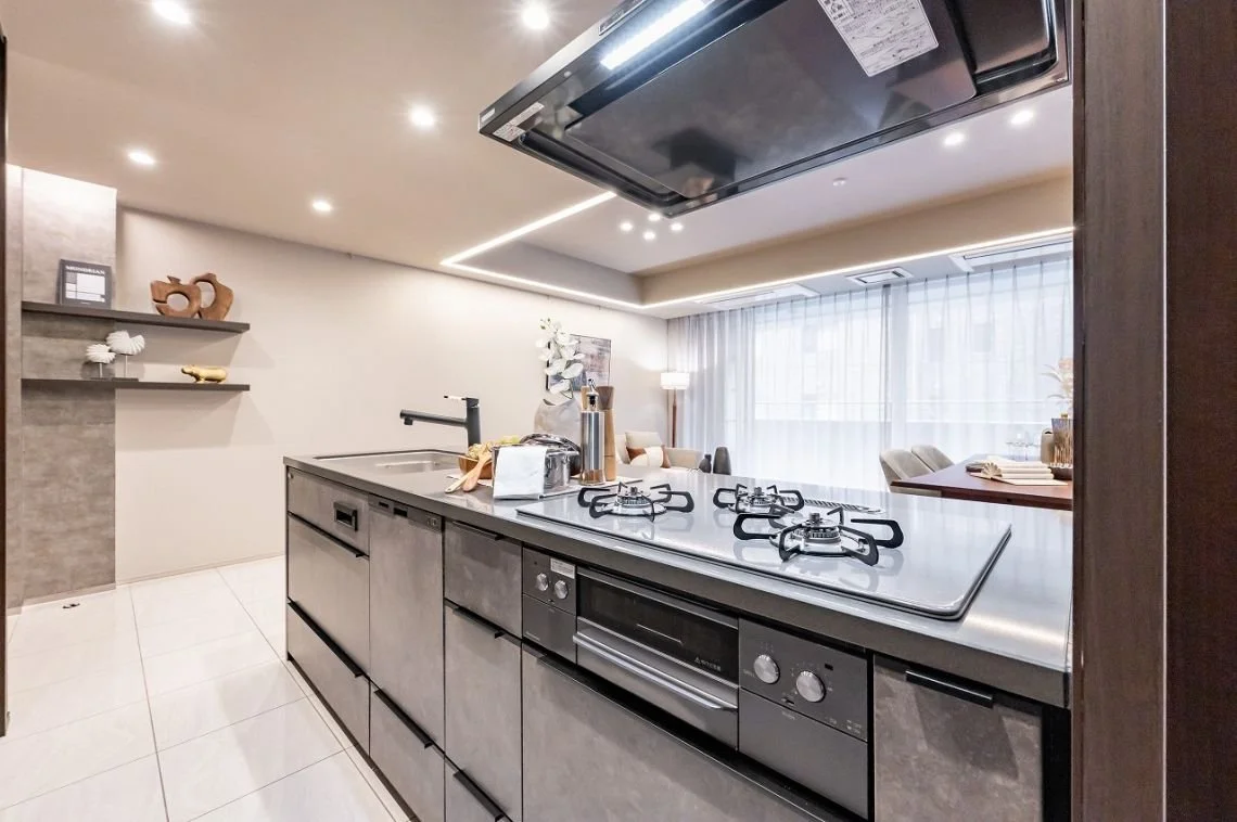 モダンなキッチンの内部。シンク、ガスコンロ、電気レンジ、大きな窓とカーテン、リビングルームが見える。