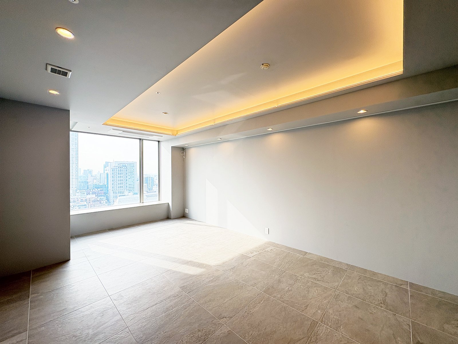 明るい高層ビルの部屋。大きな窓から都市の景色が見える。天井には間接照明。
