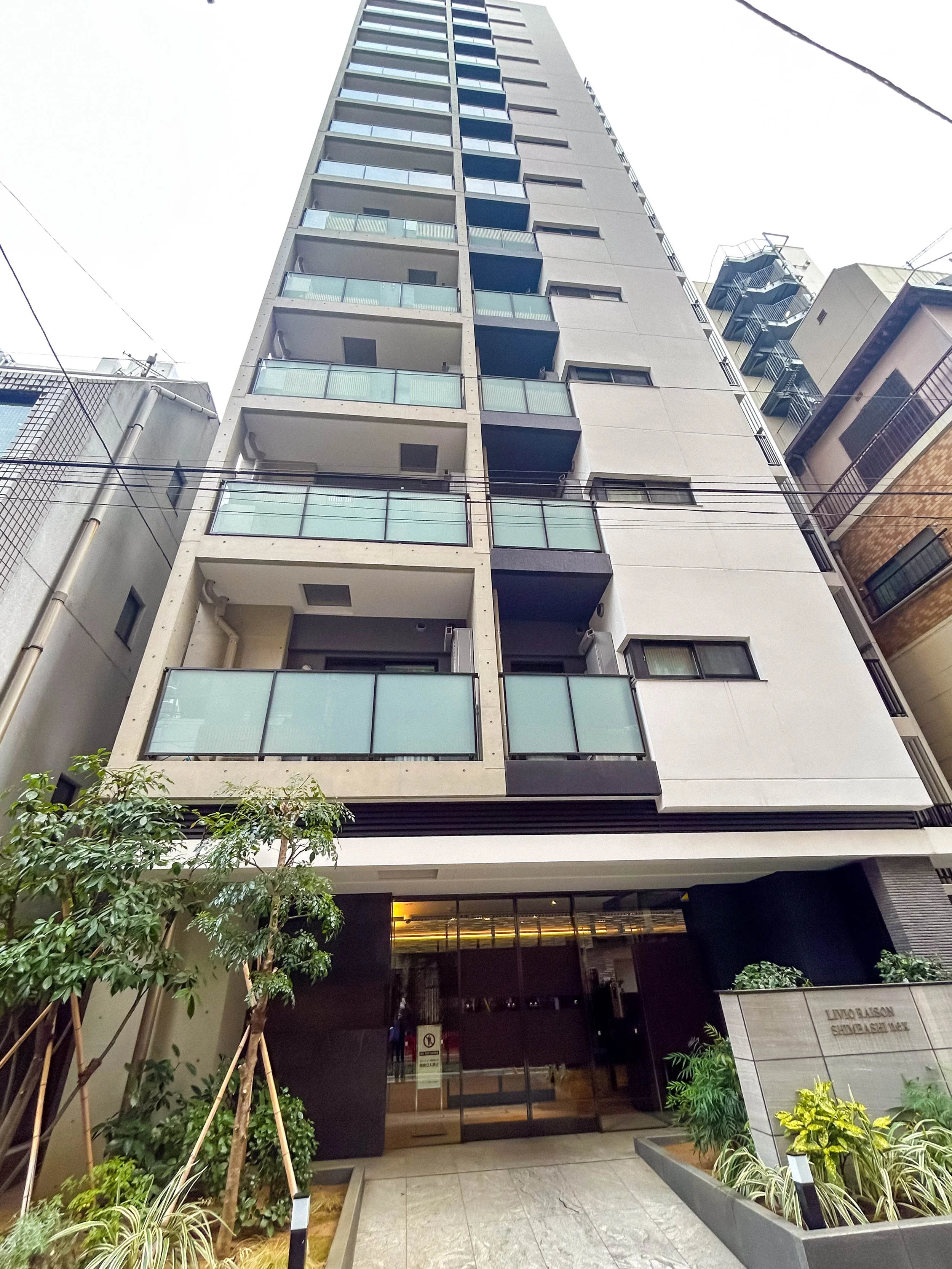 高層ビルの正面玄関。入り口には植物と案内板があり、モダンな建築デザイン。