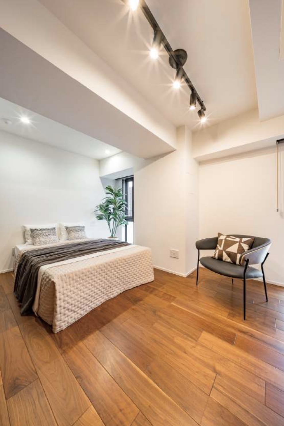 白い壁の部屋で木製の床、ベッドと椅子、観葉植物が置かれているおしゃれな室内インテリア