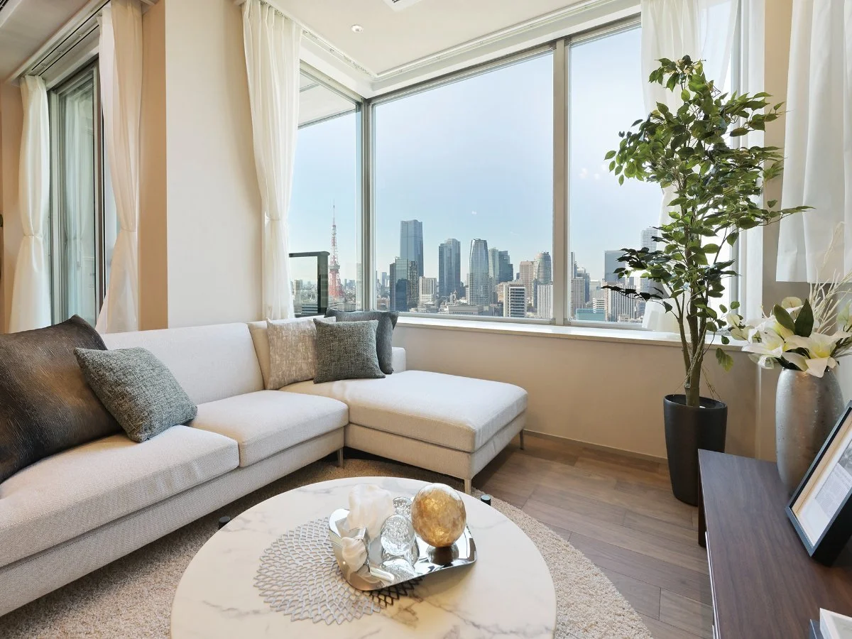 東京の高層ビル群が見えるリビングルーム。白いソファとコーヒーテーブル、観葉植物が置かれている。