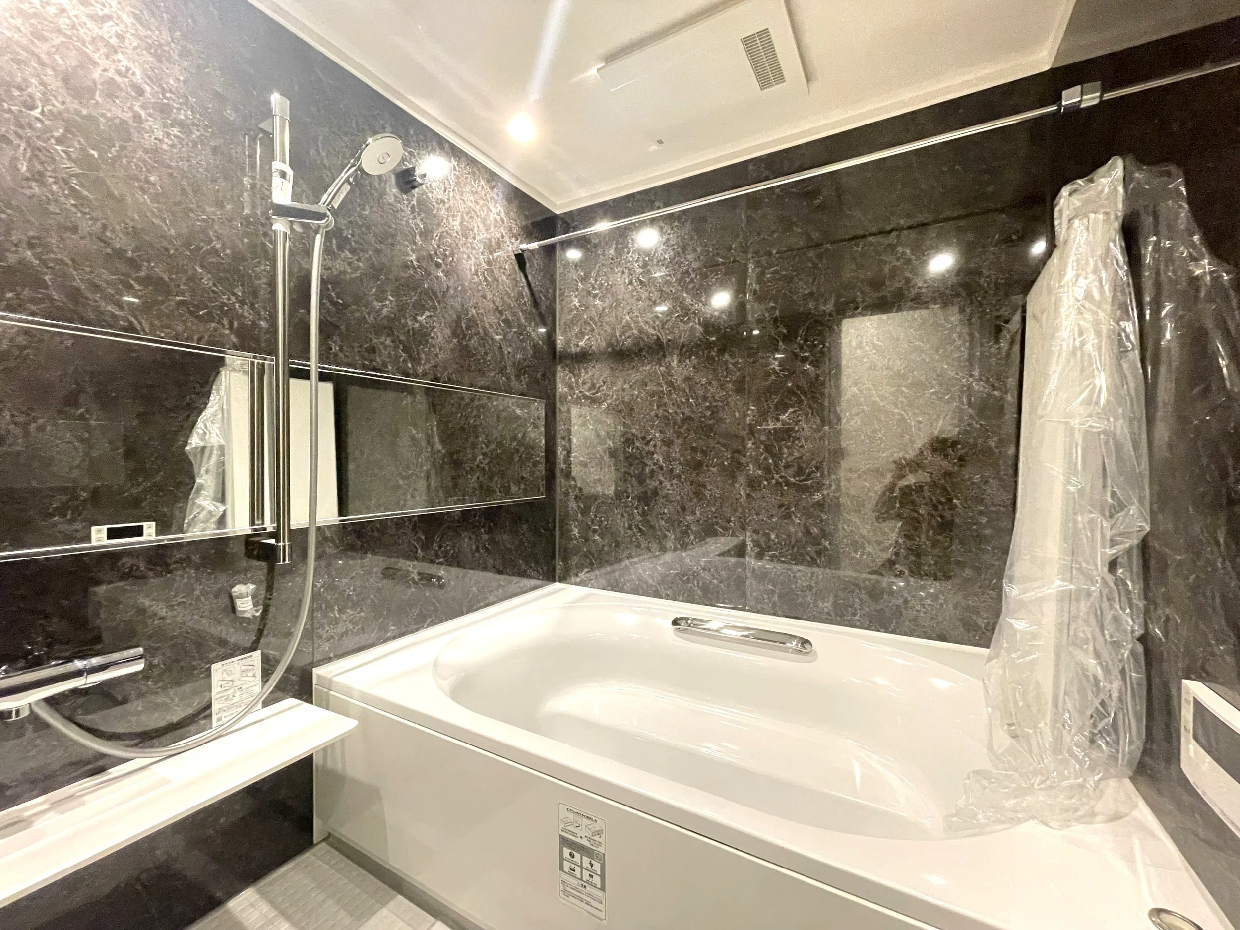 黒い大理石風の壁の浴室に白い浴槽とシャワーが設置されている。