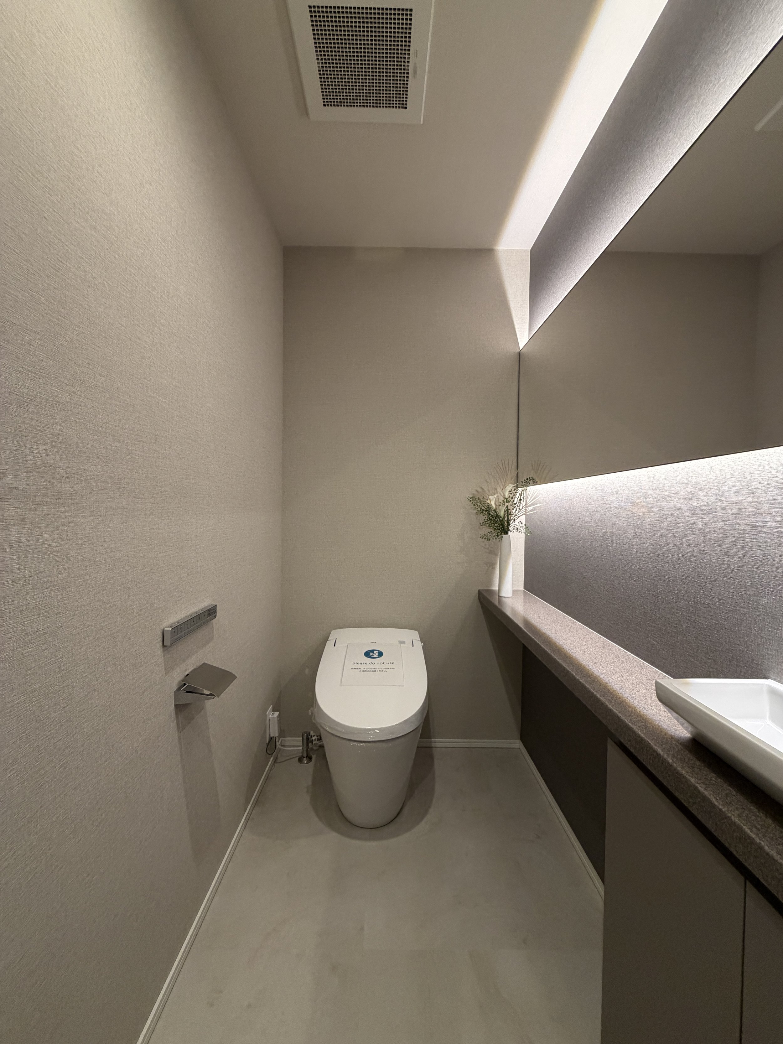 シンプルなトイレ室内、ジェット式便座とカウンターに花瓶と花が置かれている。