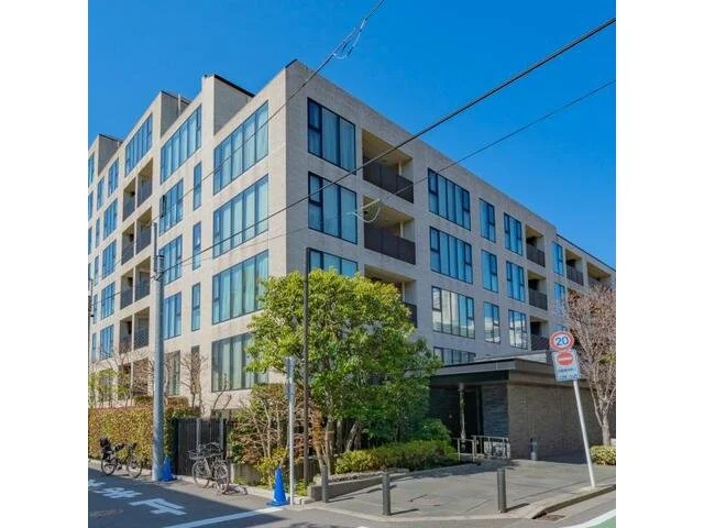 都市のマンションの外観とバルコニー、青空と木々が見える