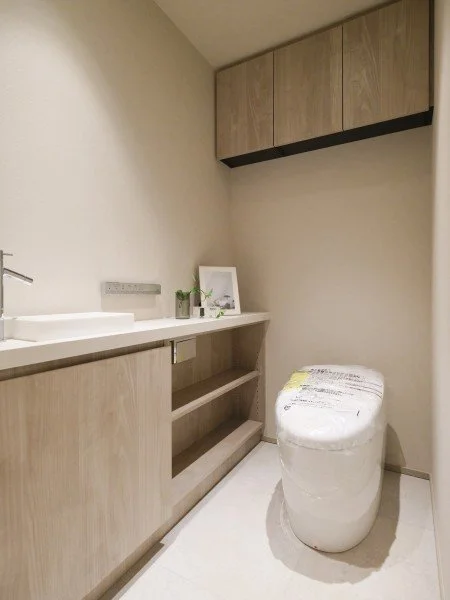 シンプルで modern な洗面所とトイレの空間。木製の収納棚とキャビネット、白い洗面台、トイレ便器が配置されている。