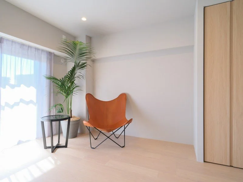 白い壁と木の床の部屋に、ブラウンの革製の椅子と、その横に大きな観葉植物、サイドテーブルが置かれている。