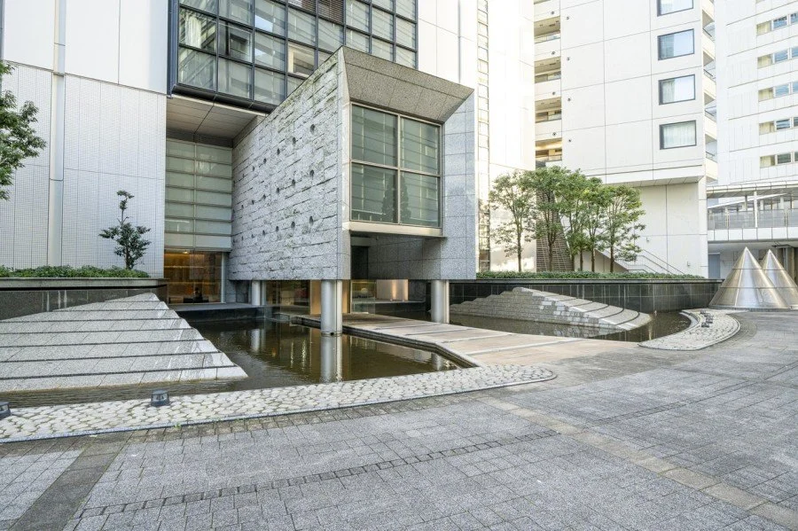 高層ビル街の中にある現代的な建築物と水の流れる庭園。ガラスと石材を使用した洗練されたデザイン。