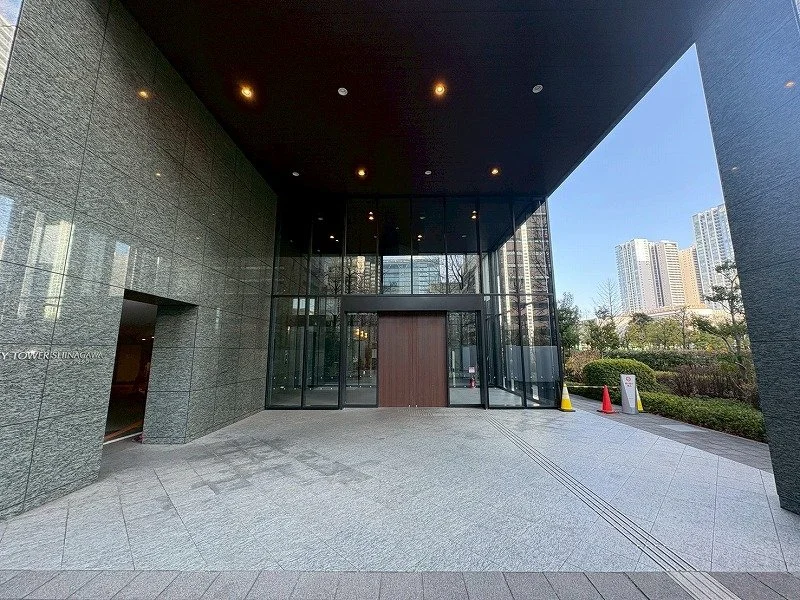 高層ビルの建物入り口のガラス扉と石壁、外に安全コーンと案内標識がある都市の風景