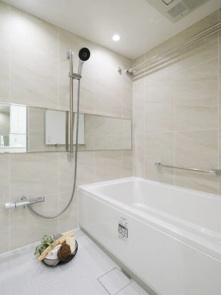 浴室の浴槽とシャワーヘッド、鏡、バスグッズが置かれた浴室の内部