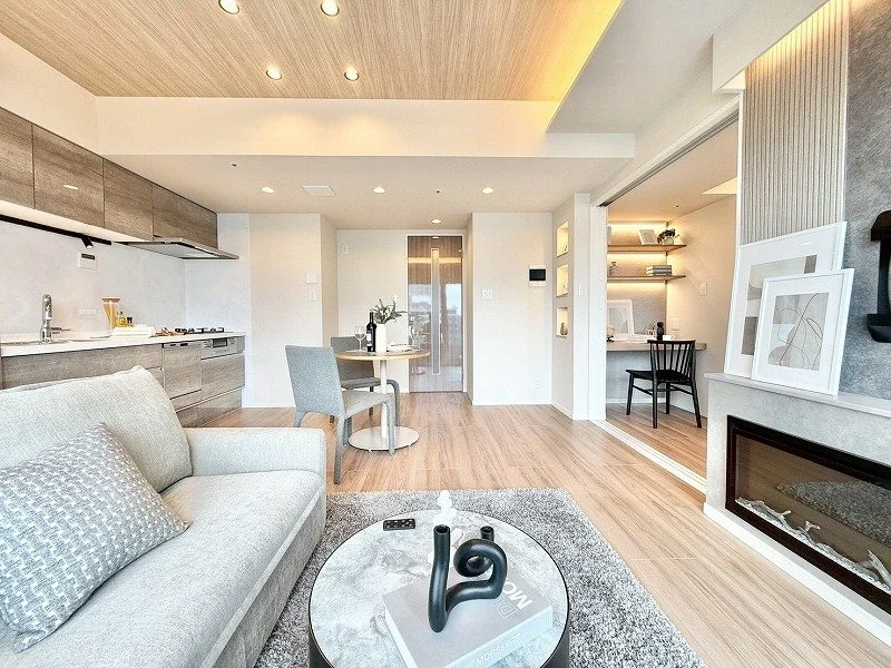 モダンなリビングルームとダイニングエリア。暖炉があり、ソファとコーヒーテーブル、ダイニングテーブルと椅子が配置されている。壁にはアート作品と本棚も見える。