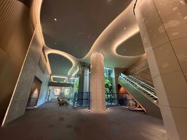 モダンな建築デザインのエントランスホール、中央に柱とガラスの壁、エスカレーターと自然光が入る大きな窓。