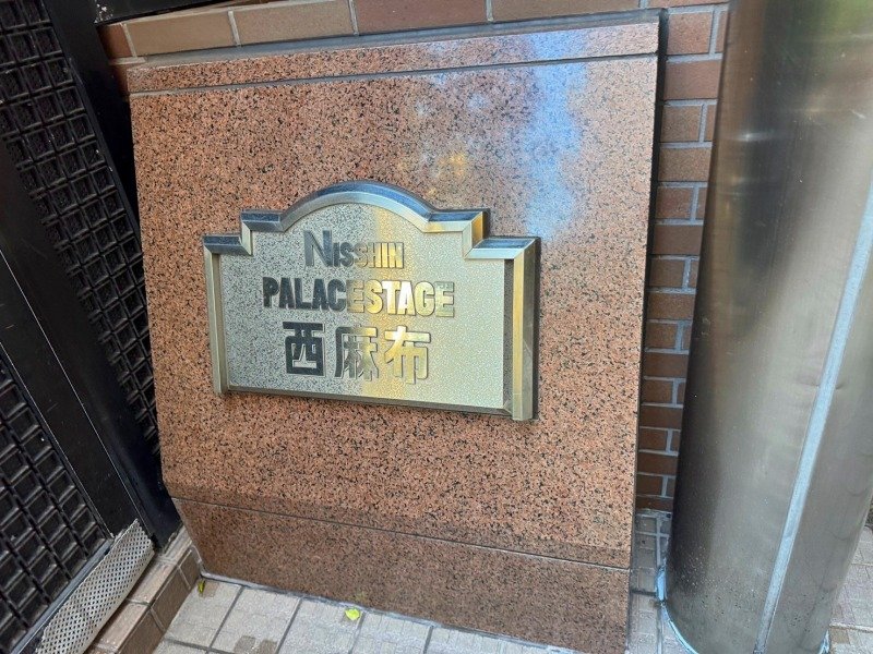 建物の壁に付けられた金属の表札で、「NISSIN PALACE STAGE」と書かれており、その下に漢字で「西麻布」と記されている。