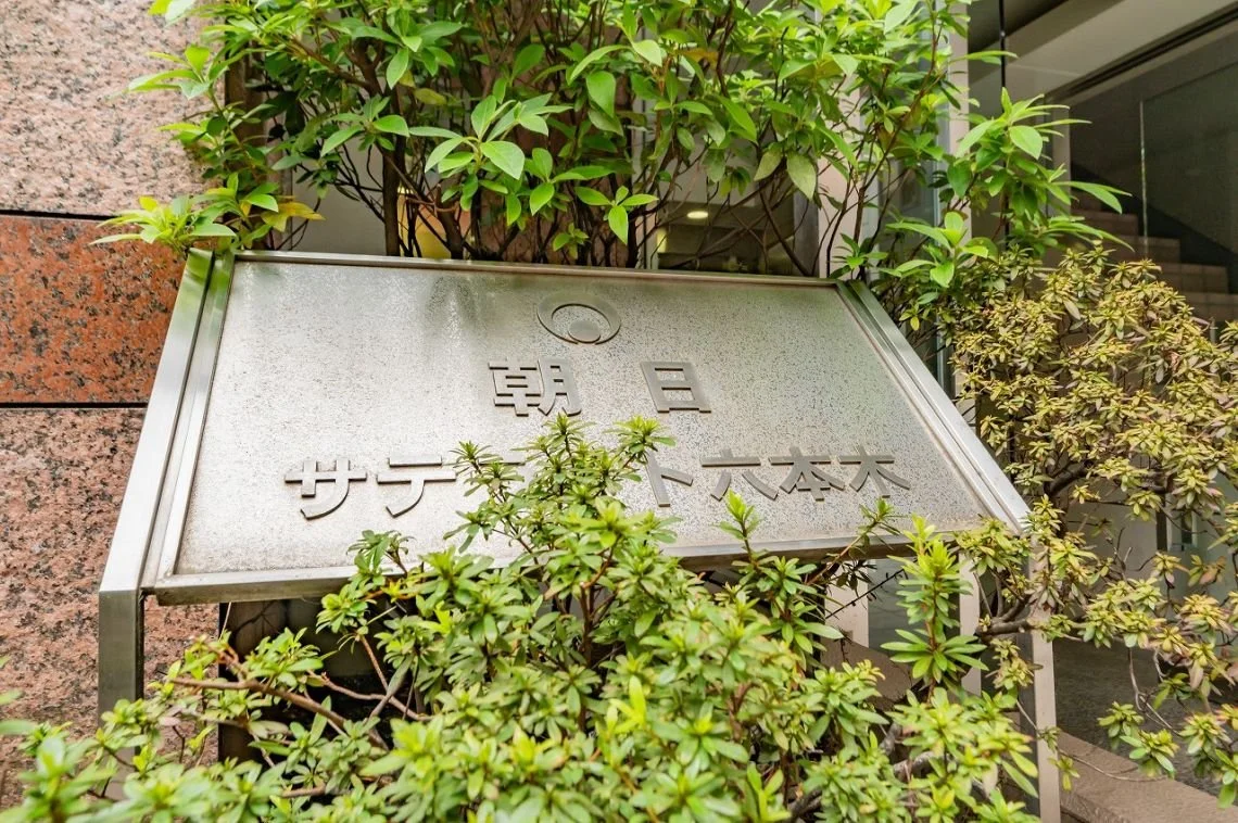 緑の植物に覆われている銀色の看板に、日本語で書かれた文字が見える。