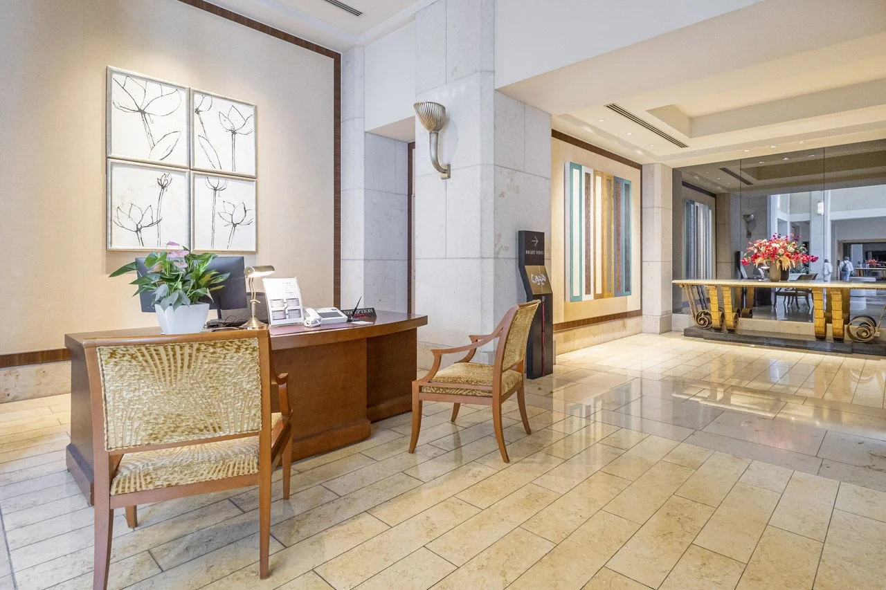 高級ホテルのロビースペース。受付カウンターと椅子、花や装飾品が配置されている。
