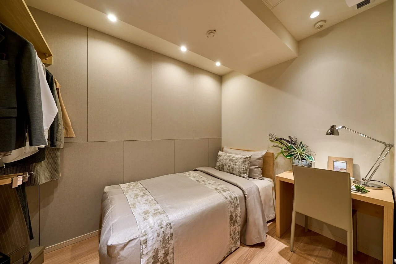 寝室のベッドとデスク。デスクにはランプと植物の飾り、写真立てが置かれている。