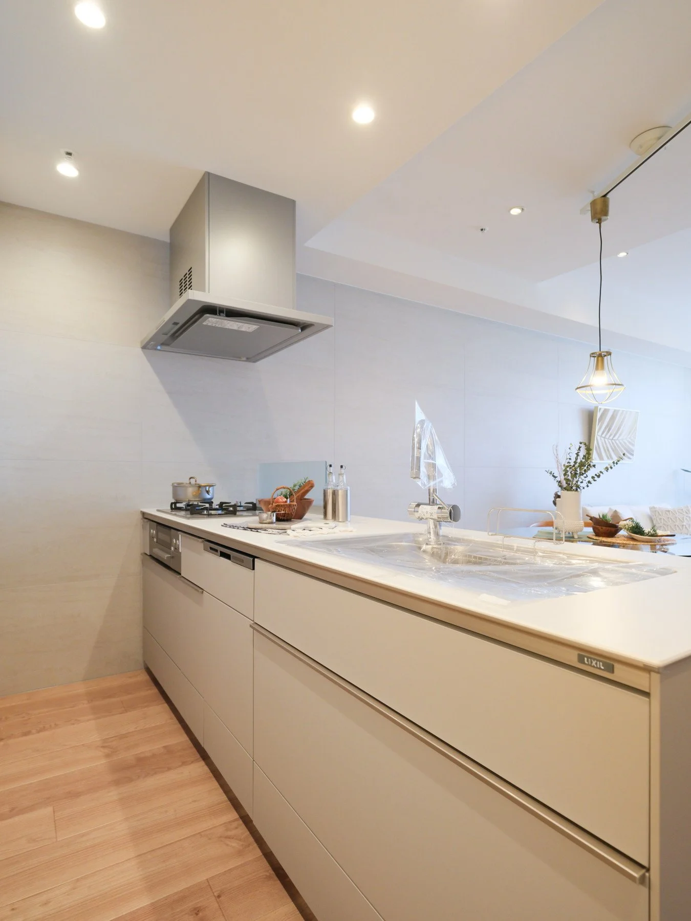 白いキッチンのカウンターとシンク、背後にコンロと換気扇、照明と装飾が施された現代的なデザイン