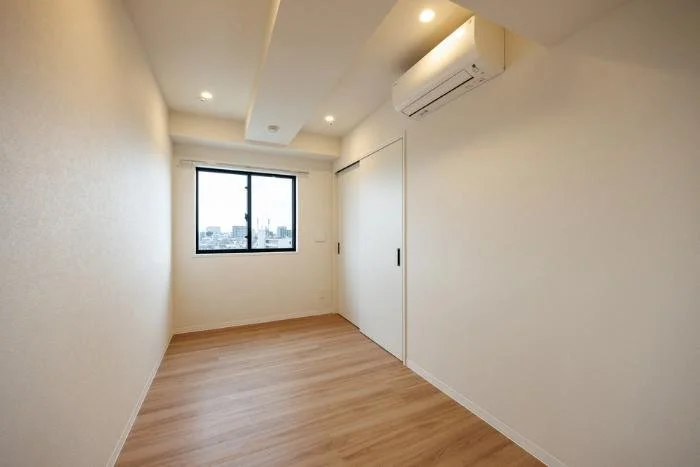 空の部屋で木製の床と白い壁、窓とエアコンがある