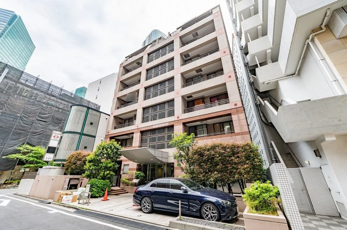 都市の高層マンションと入り口付近の車と植物