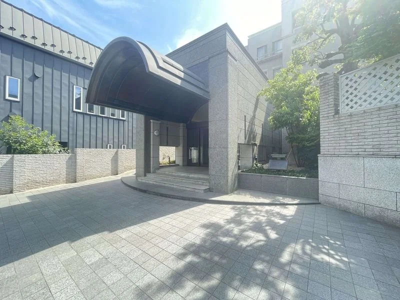 都市の建物の入口とその周囲の歩道、緑の木と日陰が見える