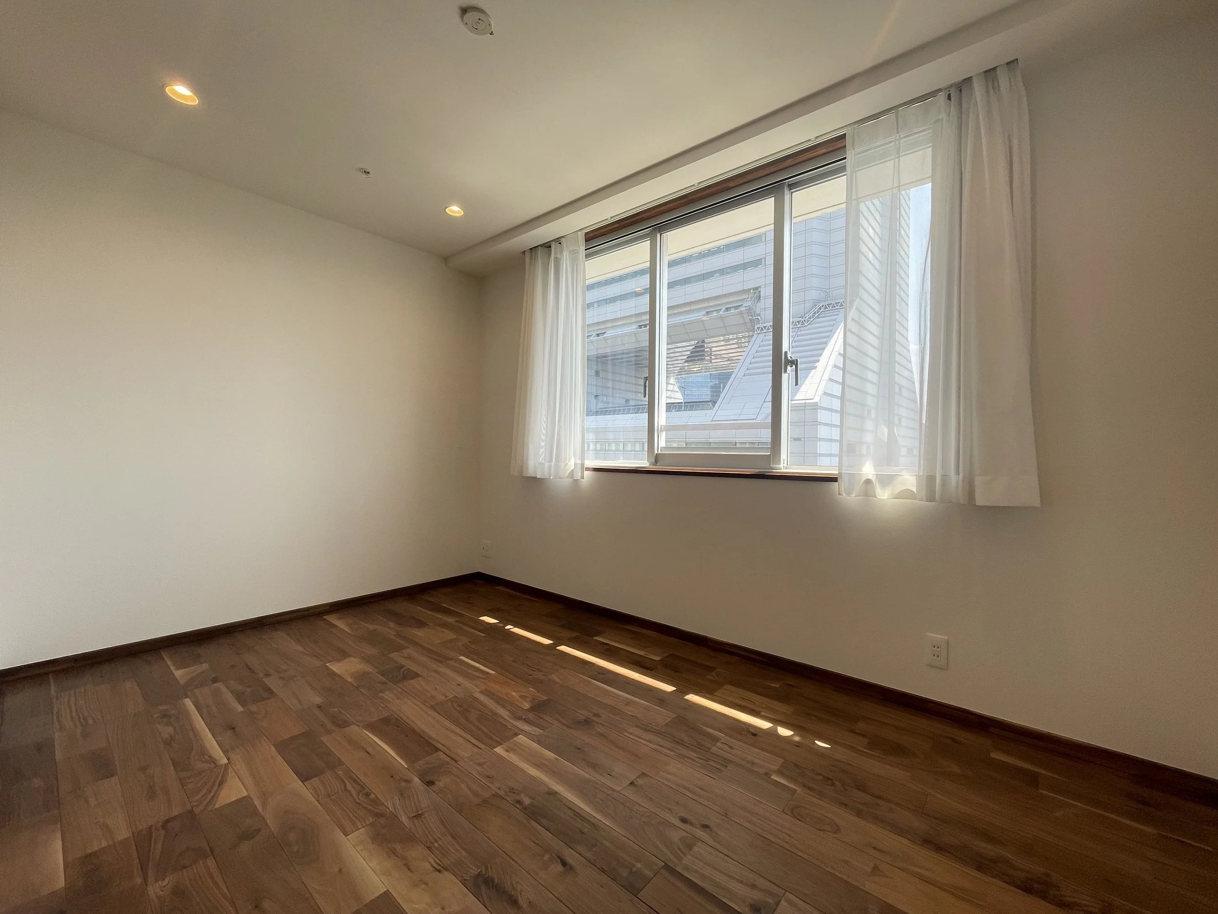 白い壁と木製の床の空室、窓から建物の外観が見える