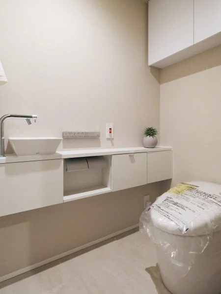 白い洗面台と収納棚、トイレットペーパー、新しいトイレ、観葉植物が置かれているトイレルームの室内