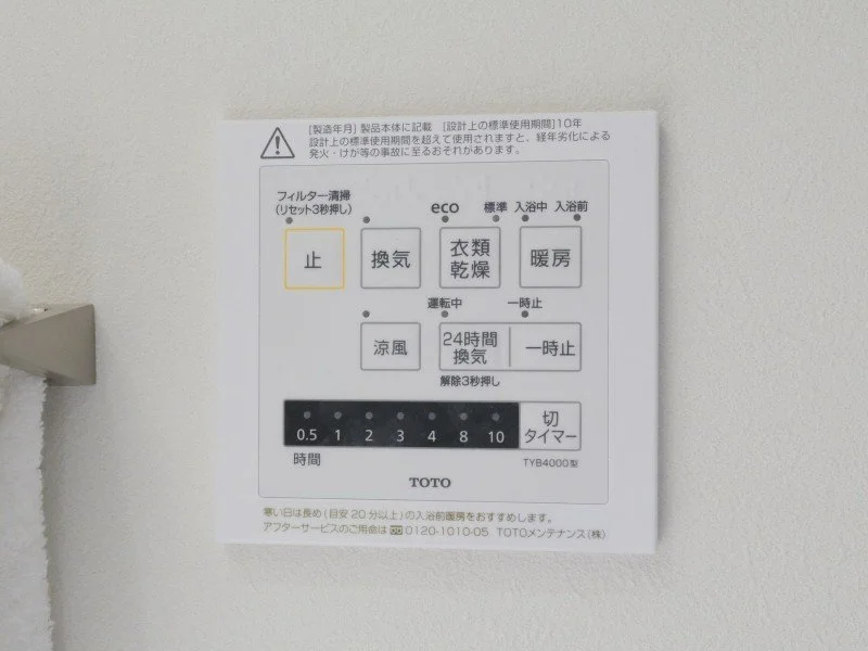 浴室の壁に貼られた操作パネルの説明書。電気毛布の設定や浴室暖房の操作ボタンや時間設定が記載されている。