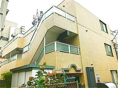 黄色い建物の外観とバルコニー、階段、植木が見える。