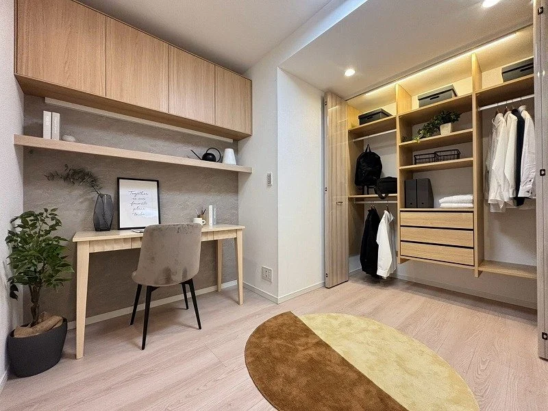 木製の壁掛け収納とデスク、植物と椅子のあるシンプルな部屋。