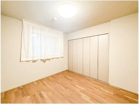 白い壁とカーテンがある空き部屋。木製の床とクローゼットも見える。