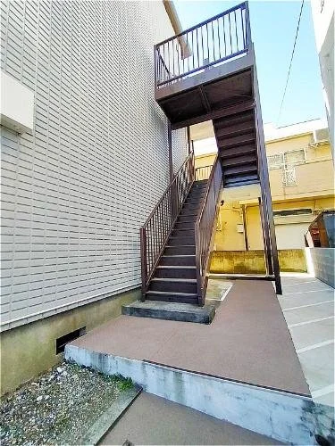鉄製の屋外階段と手すりが付いた階段室。建物の外壁と駐車場が見える。