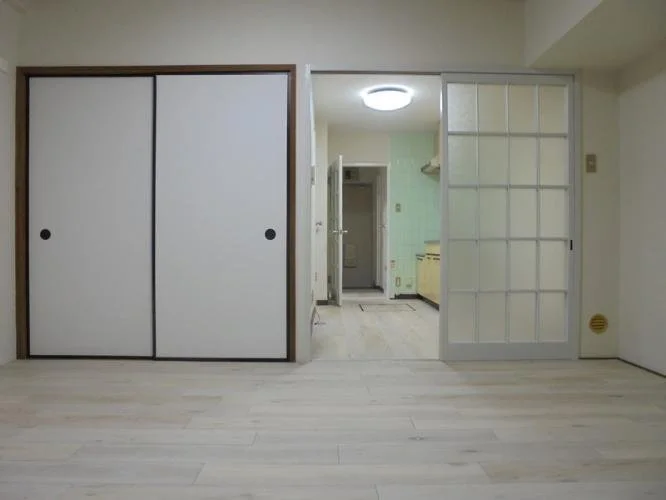空の部屋と、左側に二つ折りの白い壁紙のふすま、右側にガラス入りの引き戸がある室内写真