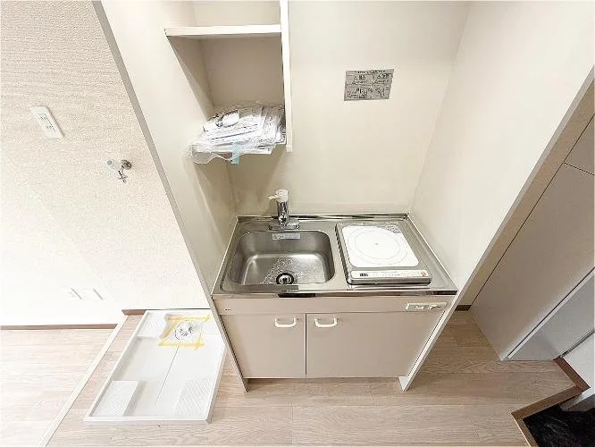 小さなキッチンエリア、シンクと電気コンロ、棚に洗濯物。