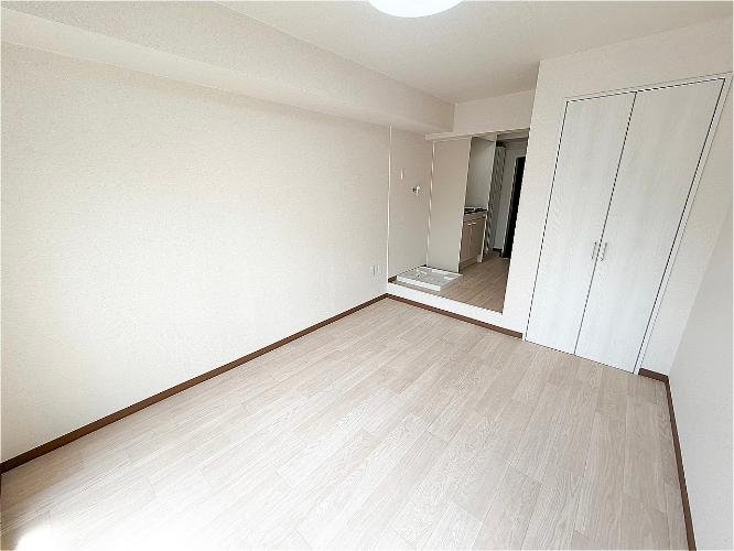 空の部屋で、壁と床が白と淡い木目調。奥にキッチンとクローゼットの扉が見える。