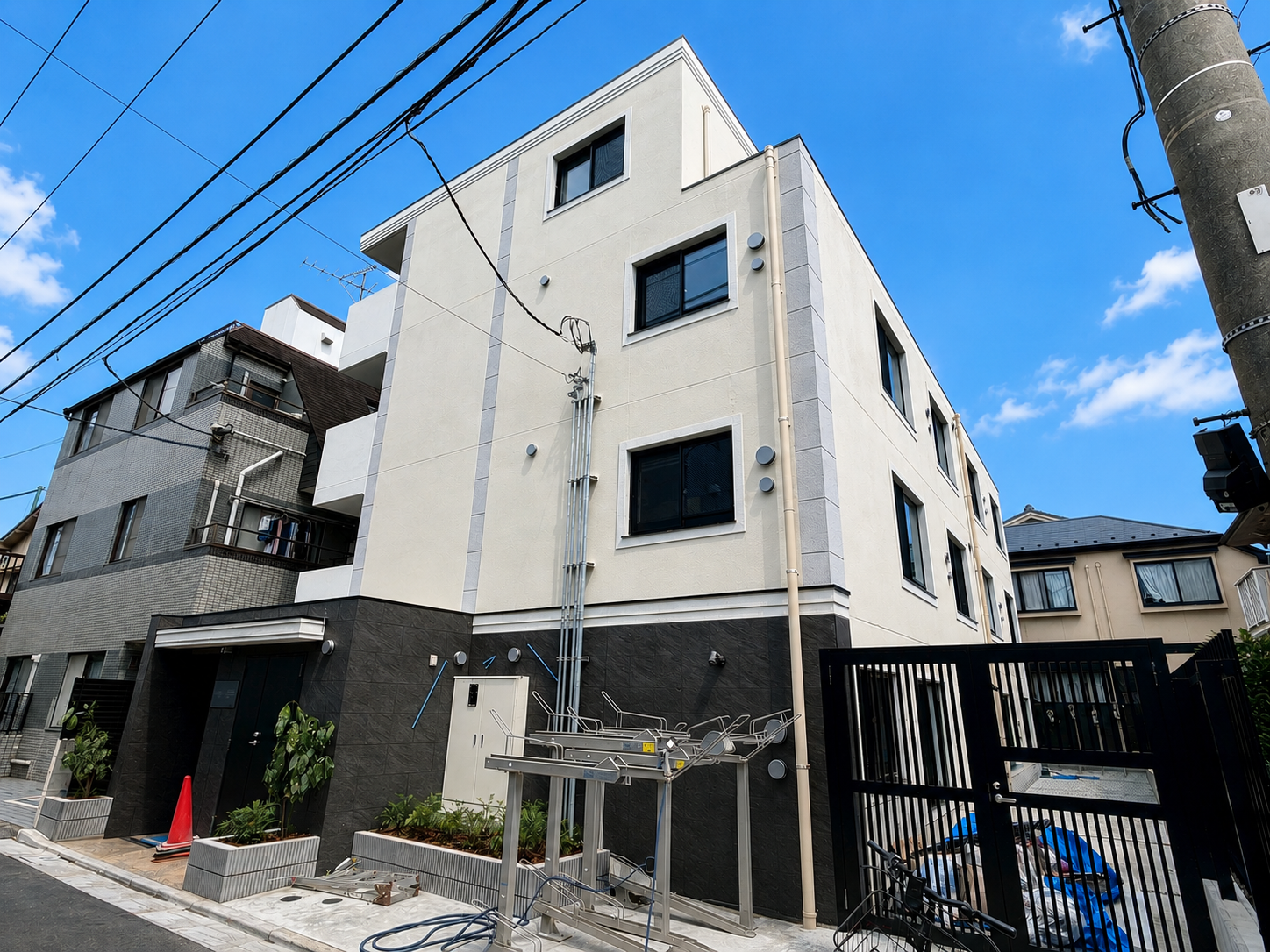 白い三階建ての住宅建築。前には植物と駐輪場。空は青く晴れている。