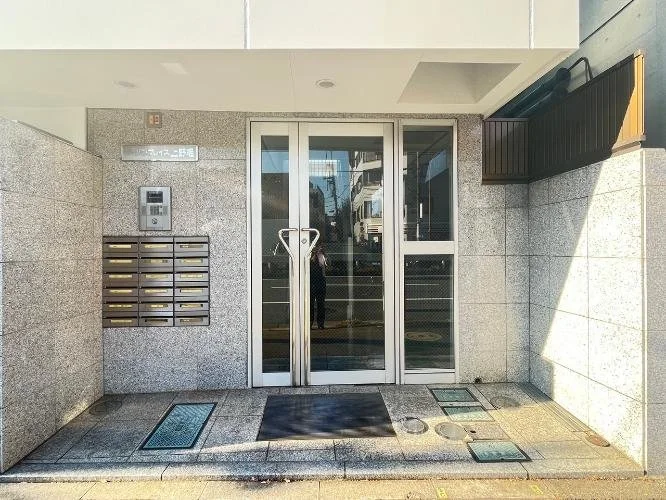 ガラスドアの建物入り口。左側に郵便箱とインターホン、それらの上に看板がある。