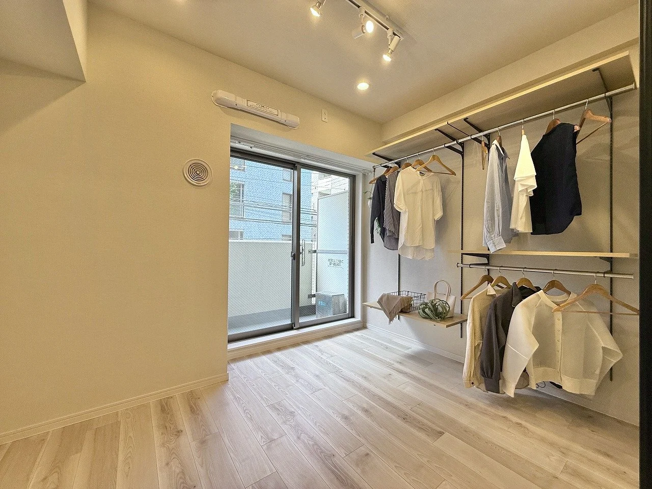 洋服を掛けたクローゼットとバルコニーのある室内の部屋