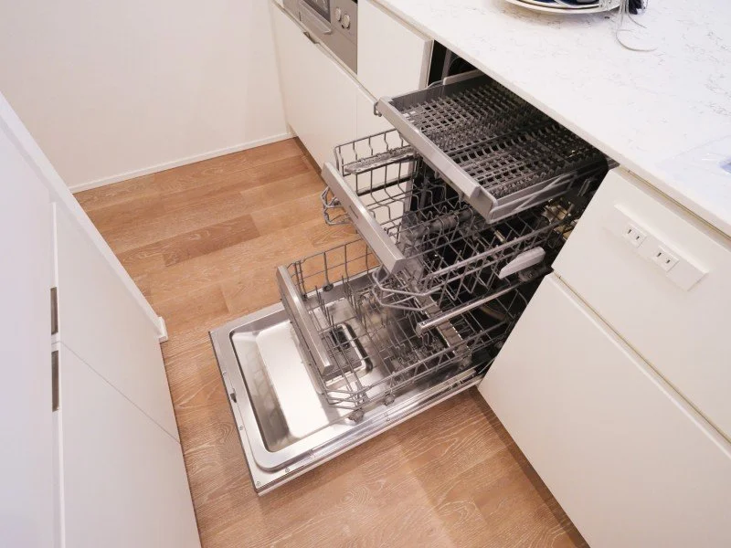 白いキッチンの引き出し式食器洗い機が開いている。中に皿や食器か洗浄ラックが見える。