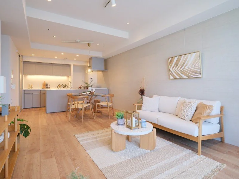 明るくシンプルなリビングルームとダイニングエリアのインテリア。木製家具と白い壁、ソファとダイニングテーブル、観葉植物や装飾が配置されている。