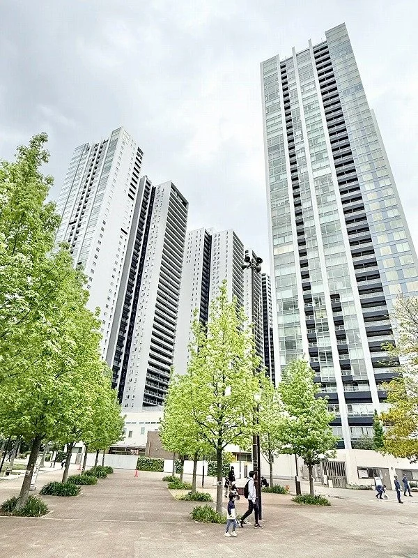 高さのある現代的な高層ビル群と、街区に植えられた緑豊かな木々。人々が歩いている。